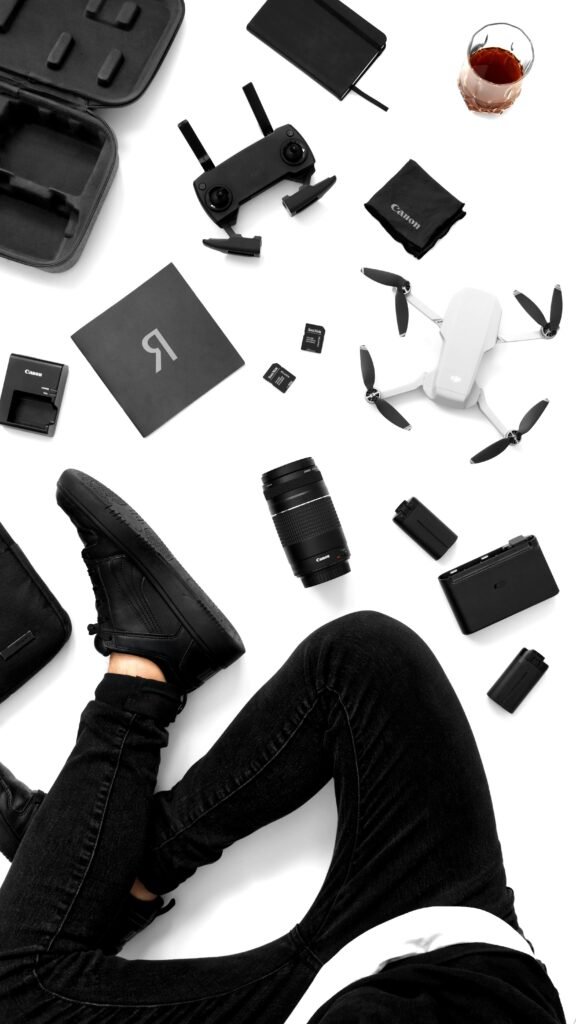 Top view of drone, camera gear, and accessories with a person in black clothing on a white background.