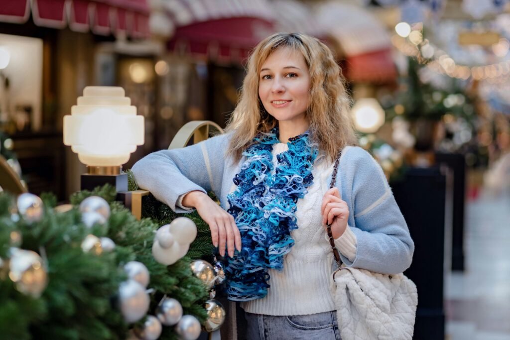 Portrait of a smiling woman in a cozy sweater surrounded by festive decorations indoors.