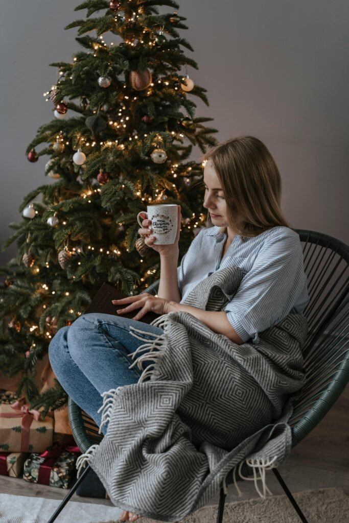 Woman relaxing with a cup by a Christmas tree, creating a cozy holiday ambiance.