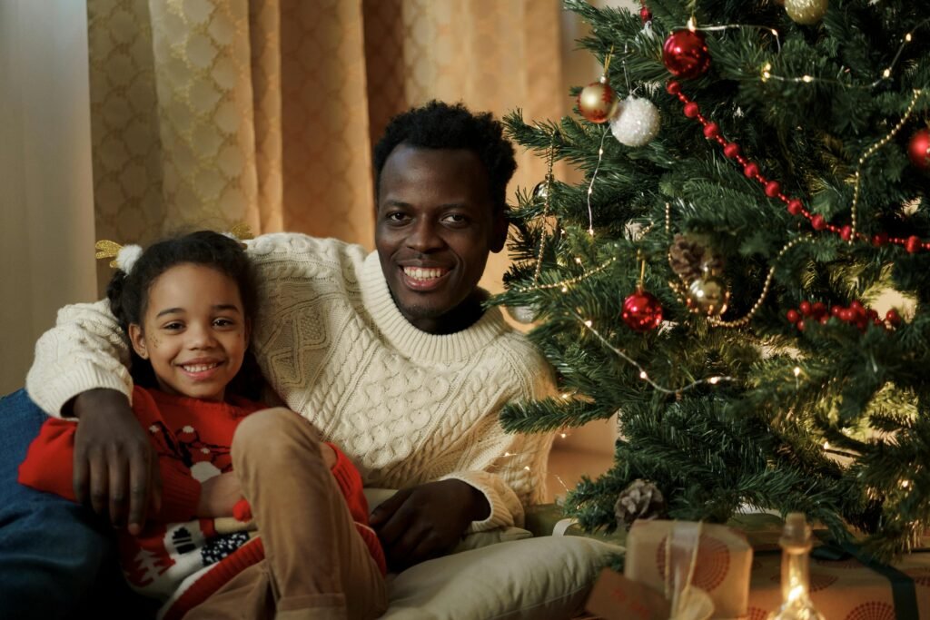 Father and daughter enjoying Christmas beside a decorated tree, sharing warmth and smiles.