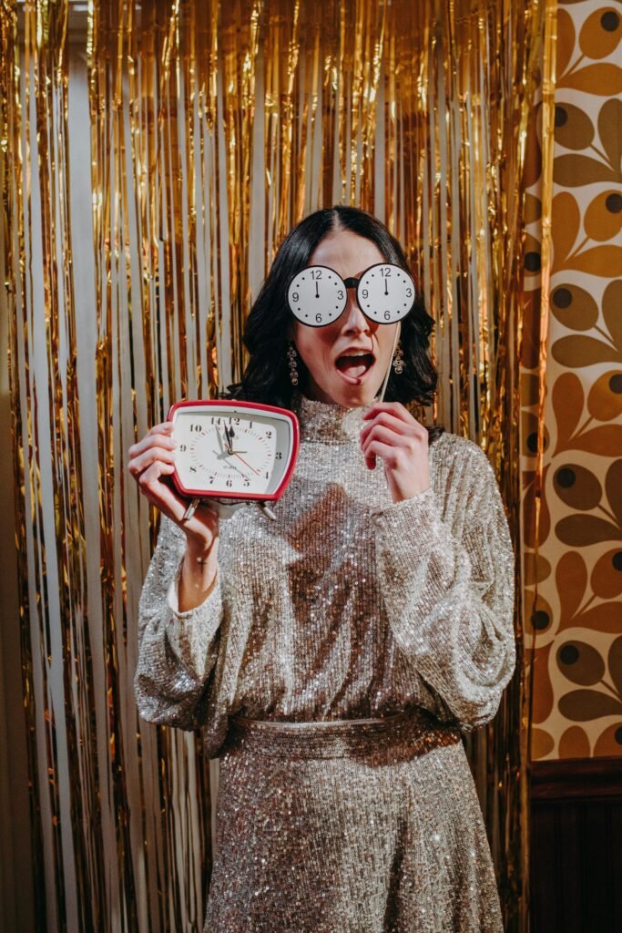 A woman in glamorous attire celebrates New Year's Eve with festive decor and clock glasses.