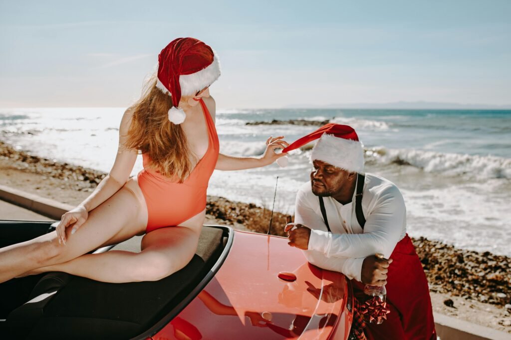 Couple enjoying a playful Christmas vacation by the sea, wearing Santa hats.