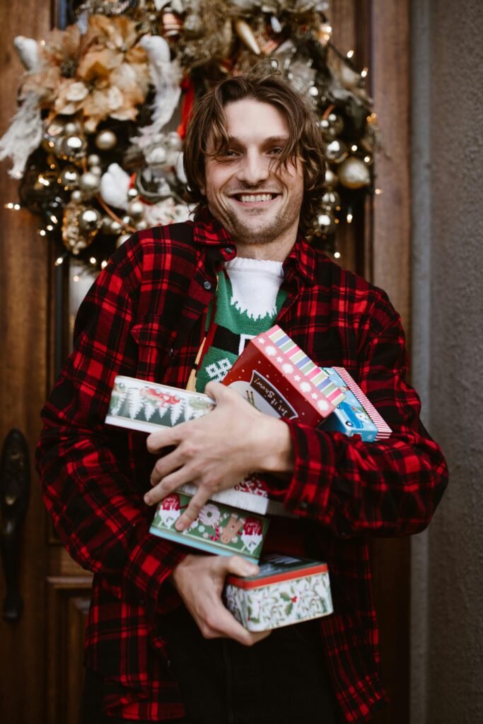 Joyful man in festive attire carrying Christmas boxes by a decorated door.