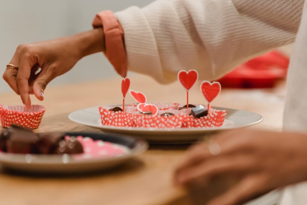 A person prepares heart-themed desserts on a wooden table for a festive celebration.