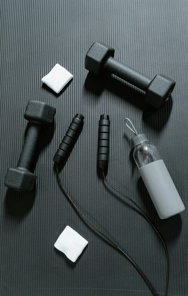 Flat lay of essential gym equipment on a yoga mat, featuring dumbbells, jump rope, and water bottle.