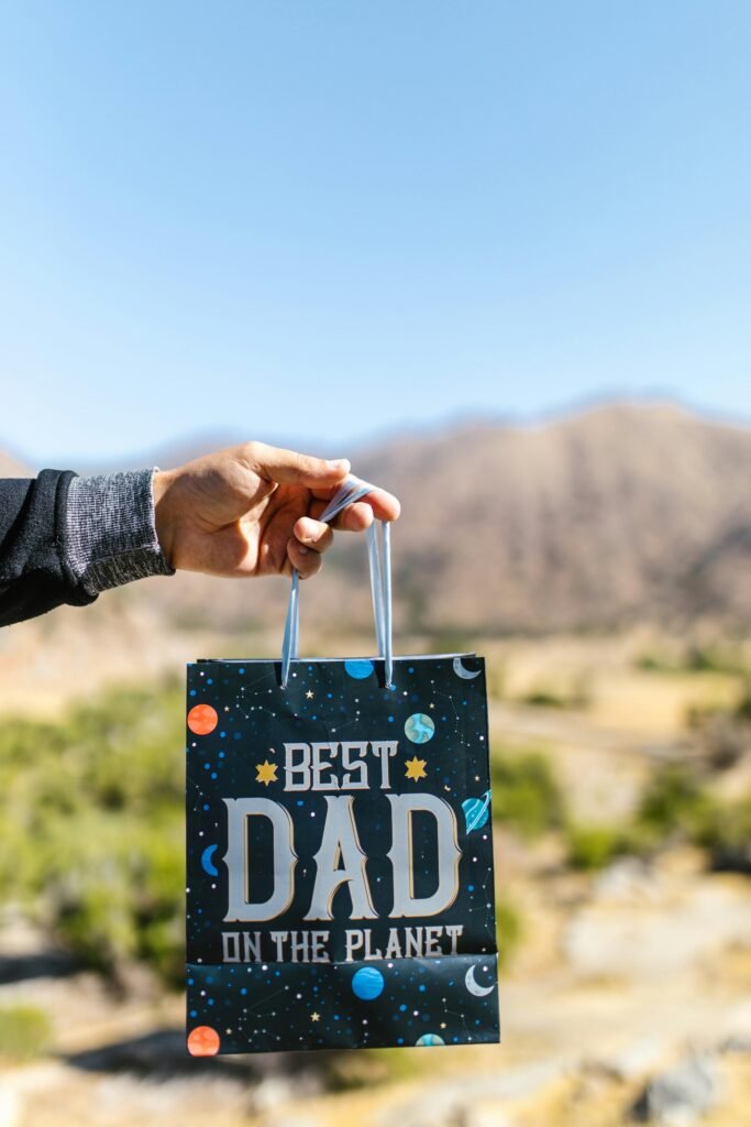 Hand holding 'Best Dad on the Planet' gift bag outdoors for Father's Day.